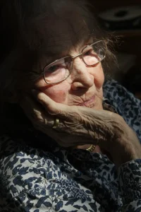 An elderly woman looking sad and outside the window.